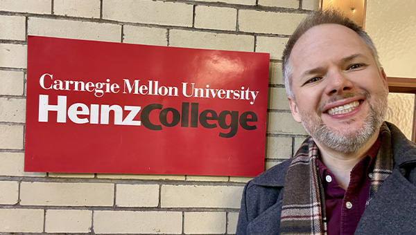 Rusty stands next to a Heinz College sign in Hamburg Hall.