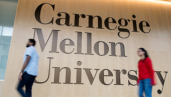 Two students pass by the large Carnegie Mellon University sign on the wall of the visitors' center in Tepper.